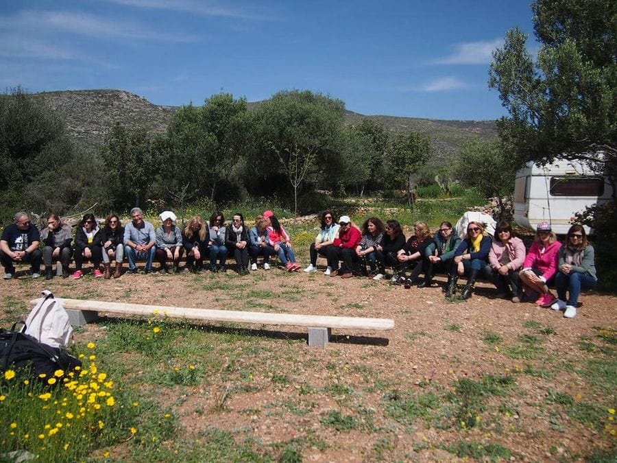 group of tourists smile happily at the camera and sitting on low wooden benches surrounded by trees at Korogonas Ark